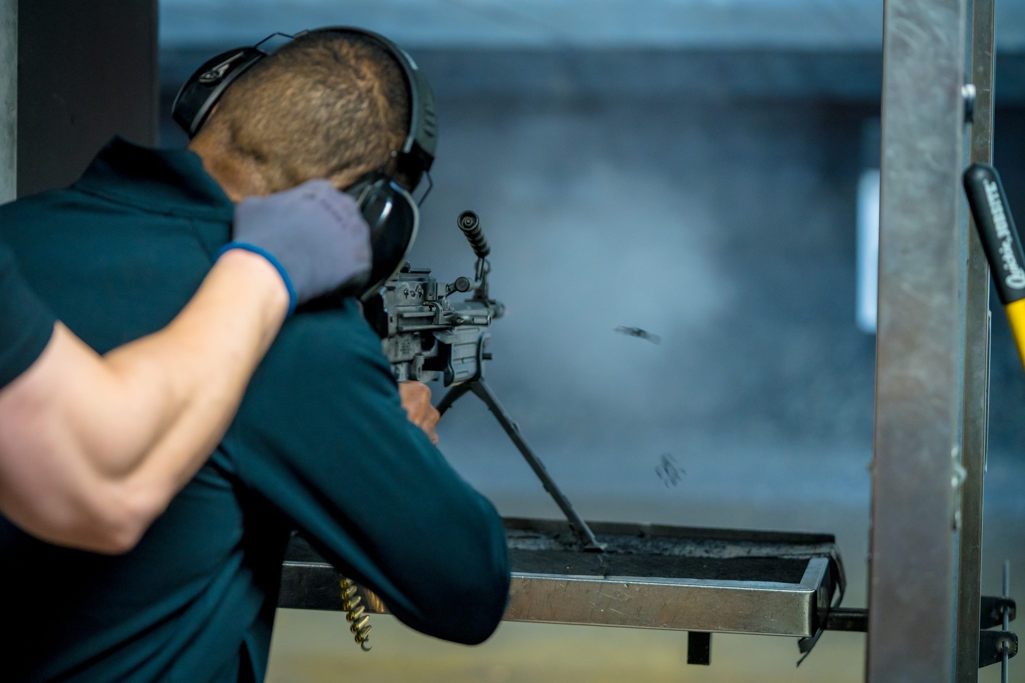 A guest in ear protection fires a belt-fed machine gun from a bench mount in an indoor lane at Machine Guns Vegas